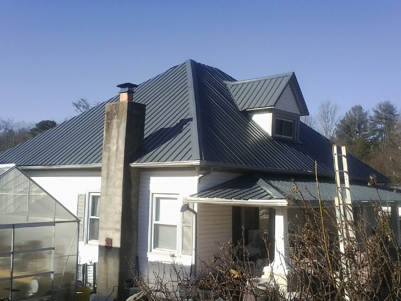 Dark blue standing seam metal roof on a white farmhouse with dormer — Slate & Tile Roof Repair by Roofing Brothers in Emerald Isle