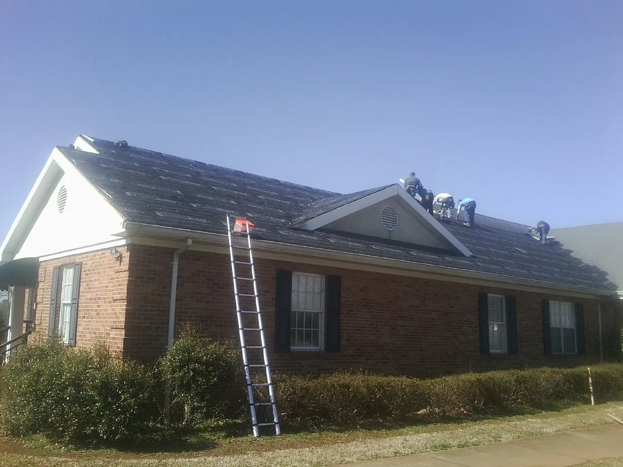Crew tearing shingles off a brick ranch roof with a ladder set — Emergency Roof Repair work by our crew in Emerald Isle