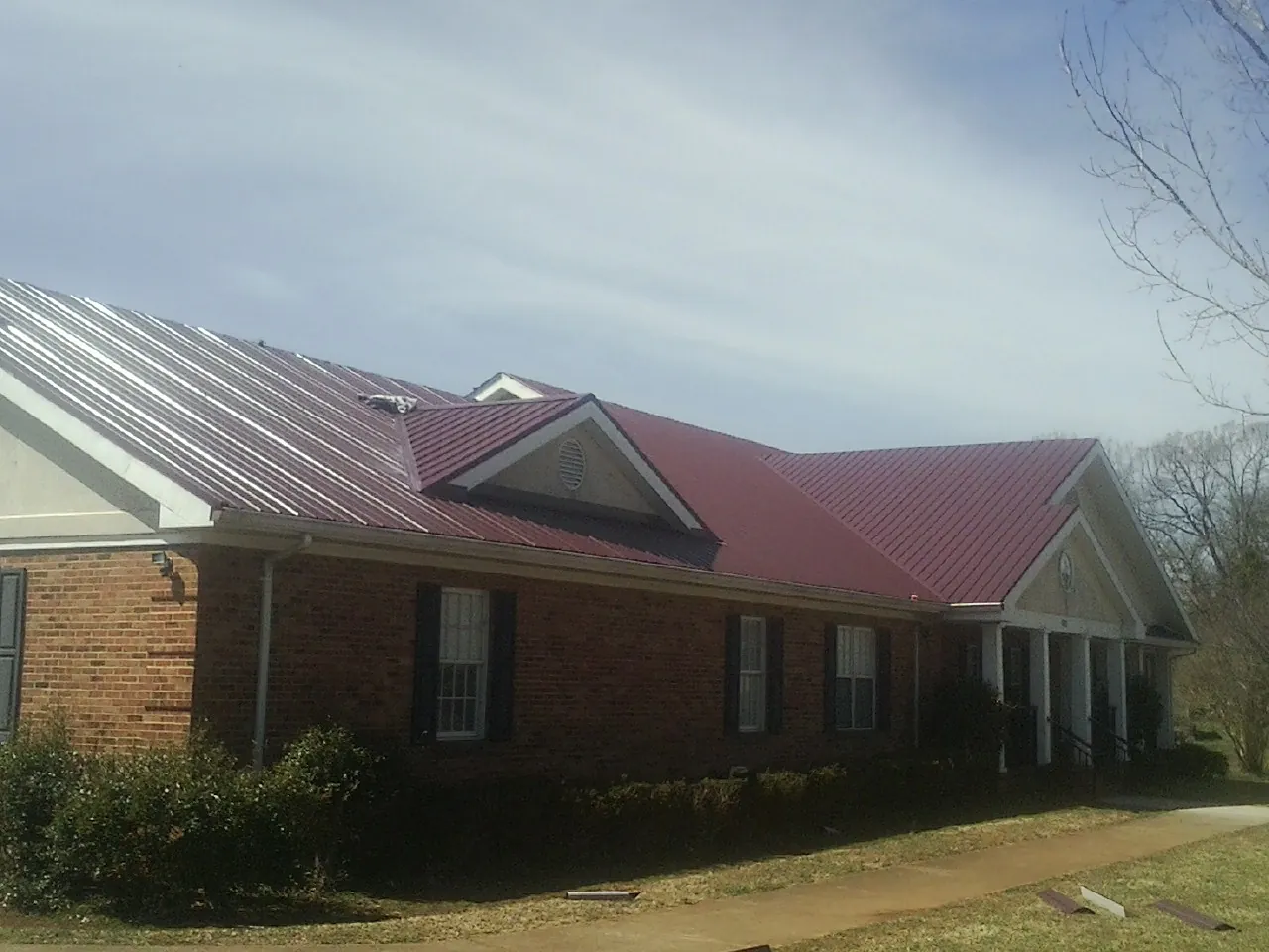 Red metal roof with gabled entries on a long brick building, from a Hail Damage Roof Repair job in Emerald Isle