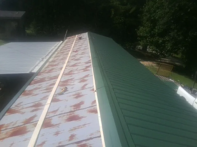 Old rusted panels beside newly installed green metal roofing — Wind Damage Roof Repair by Roofing Brothers in Emerald Isle
