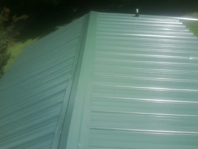 New green metal panels meeting at the ridge of a roof — Flat Roof Repair work by our crew in Emerald Isle