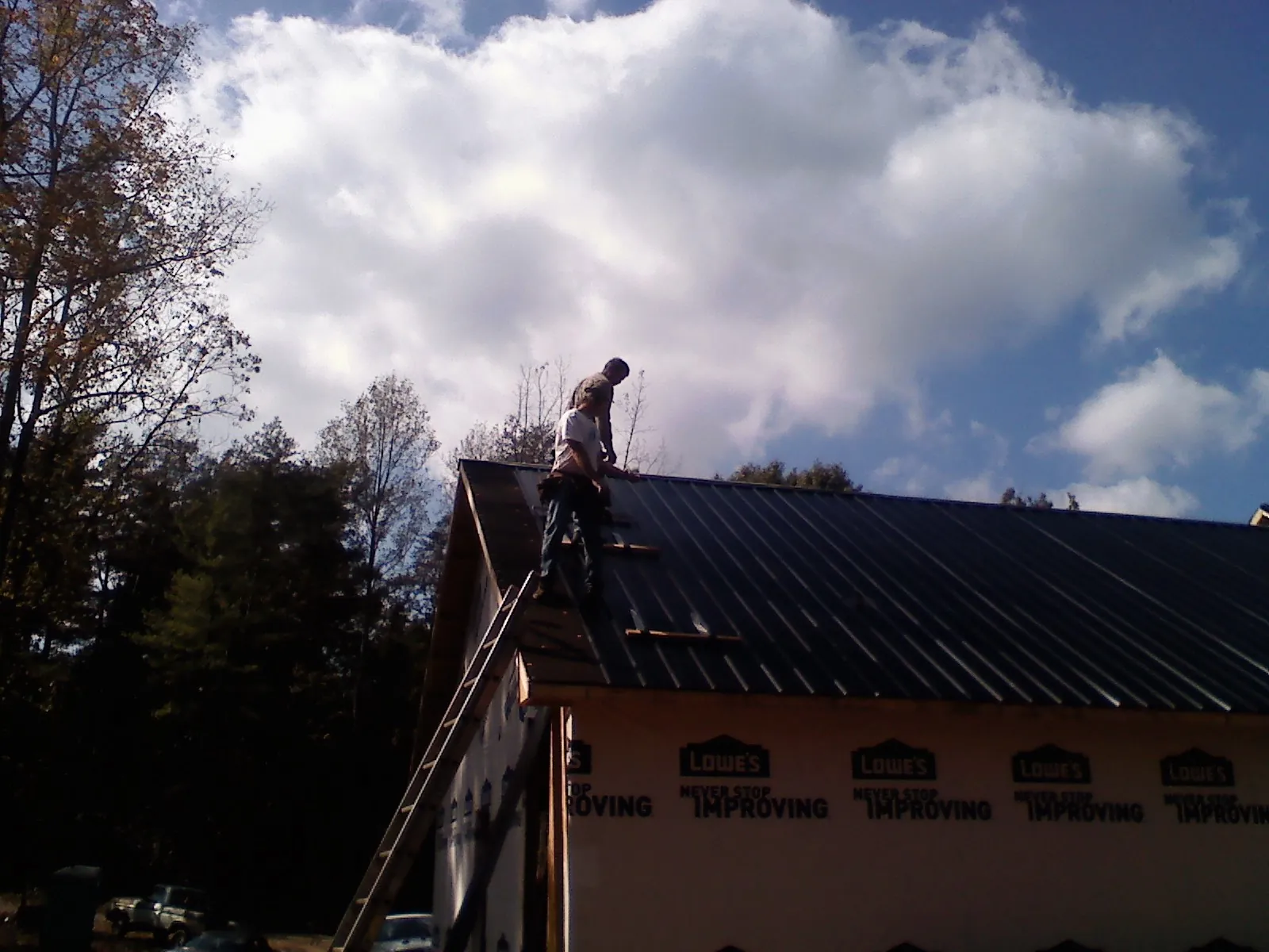 Roofer fastening dark metal panels high against a cloudy sky, from a Roof Inspection job in Emerald Isle