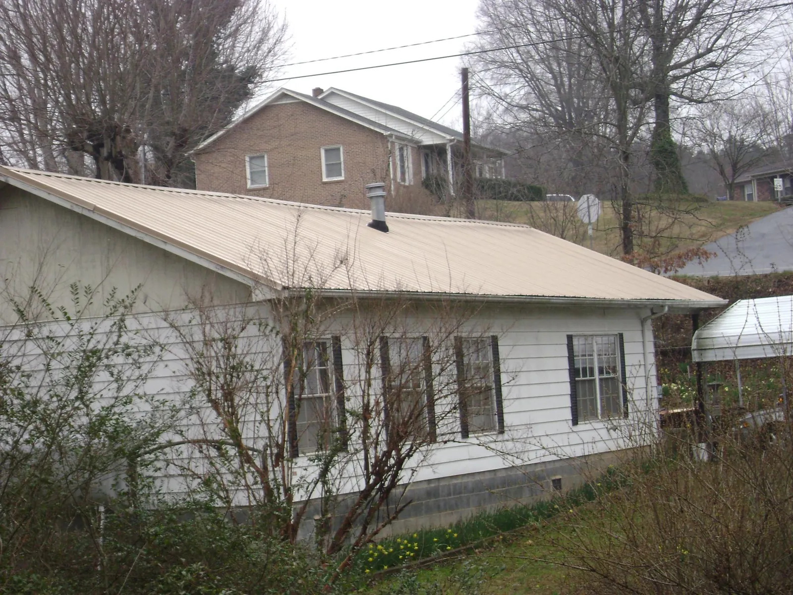 Tan metal roof on a white sided house set into a hillside — Commercial Roofing by Roofing Brothers in Emerald Isle