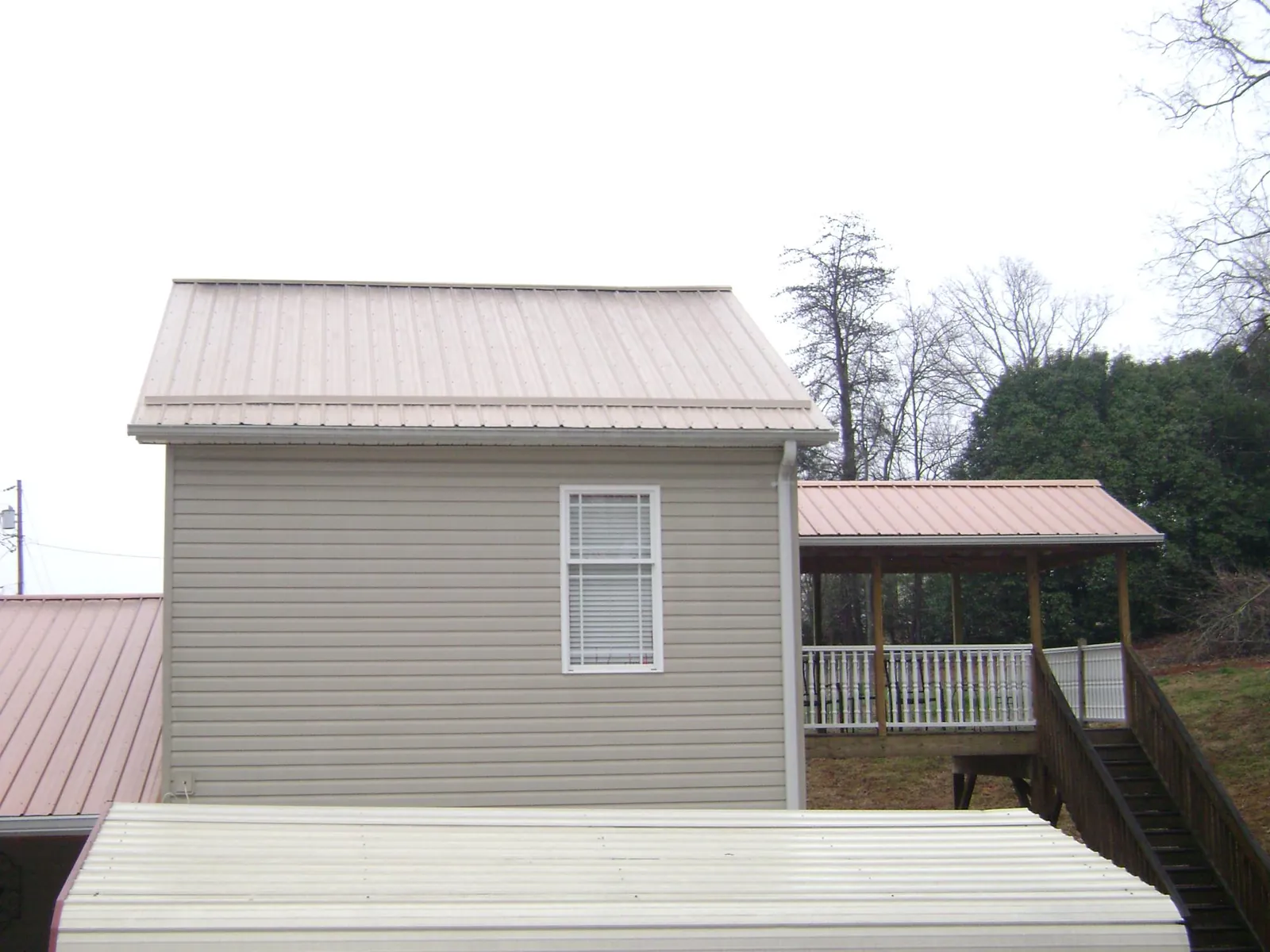 Tan metal roofs on a two story addition and attached porch, from a Roof Replacement job in Emerald Isle